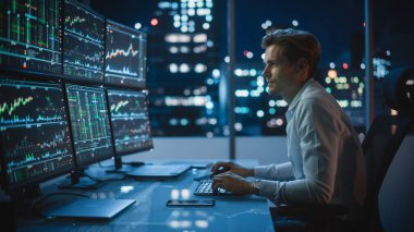 Finansal Analizci, Multi-Monitor Workstation ve Real-time Borsa ve Borsa Çizelgeleri ile bir bilgisayar üzerinde çalışıyor. İşadamı Yatırım Bankası Şehir Merkezi Ofisinde Gece Çalışıyor.