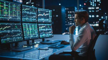 Finansal Analizci, Multi-Monitor Workstation ve Real-time Borsa ve Borsa Çizelgeleri ile bir bilgisayar üzerinde çalışıyor. İşadamı Yatırım Bankası Şehir Merkezi Ofisinde Gece Çalışıyor.