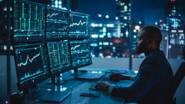 Gerçek zamanlı hisse senetleri, emtialar ve borsa grafikleri ile birlikte Multi-Monitor Workstation ile bilgisayar üzerinde çalışan finansal analist. Afrikalı Amerikalı Tüccar Yatırım Bankası 'nda Gece Geç Saatlere Kadar Çalışıyor.