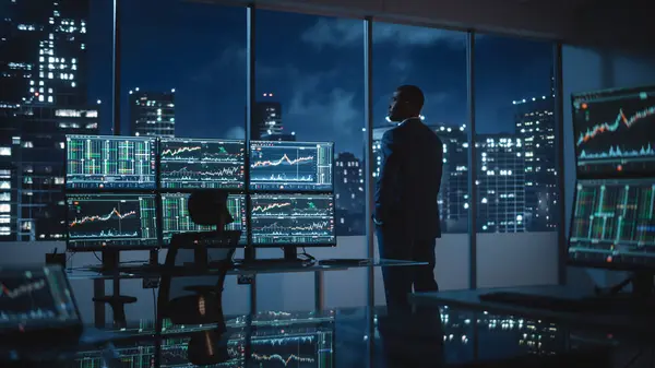 成功的商人在深夜向窗外张望 配备计算机的现代对冲基金办公室 配备实时股票 大宗商品和外汇市场图表的多监控工作站 — 图库照片