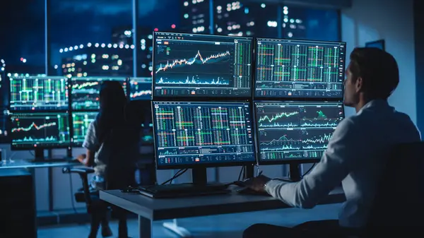 Finansal Analizci Multi-Monitor Workstation ve Real-time Stocks, Commodities ve Foreign Exchange Charts ile bir bilgisayar üzerinde çalışıyor. Yatırım Bankası Şehir Ofisinde Gece İşadamı Çalışıyor.