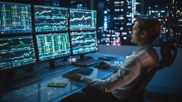 Finansal Analizci Multi-Monitor Workstation ve Real-time Stocks, Commodities ve Foreign Exchange Charts ile bir bilgisayar üzerinde çalışıyor. Yatırım Bankası Şehir Ofisinde İşadamı Gece Geç Saatlere Kadar Çalışıyor.