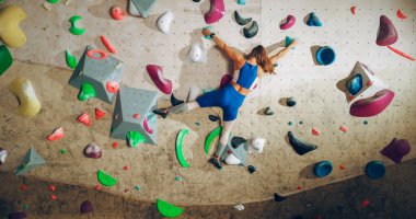 Sporcu Kadın Kaya Tırmanışçısı Spor Salonunda Tek başına Bouldering Wall 'a tırmanıyor. Kapalı Spor Salonu 'nda Kadın Egzersizleri Sağlıklı Yaşam Tarzı Eğitimi İçin Aşırı Spor Yapıyor. Arkadan çekim.