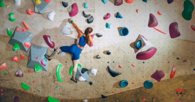 Sporcu Kadın Kaya Tırmanışçısı Spor Salonunda Tek başına Bouldering Wall 'a tırmanıyor. Kapalı Spor Salonu 'nda Kadın Egzersizleri Sağlıklı Yaşam Tarzı Eğitimi İçin Aşırı Spor Yapıyor. Arkadan çekim.
