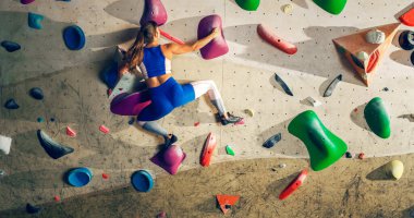 Sporcu Kadın Kaya Tırmanışçısı Spor Salonunda Tek başına Bouldering Wall 'a tırmanıyor. Kapalı Spor Salonu 'nda Kadın Egzersizleri Sağlıklı Yaşam Tarzı Eğitimi İçin Aşırı Spor Yapıyor. Arkadan çekim.