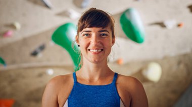 Rock Climbing Gym 'de gülümseyen ve poz veren güzel bayan sporcu ile Kayalık Duvar Arka planı. Çekici, kendine güvenen, spor yapan mutlu esmer kadın. Sağlıklı Yaşam Tarzı Portresi.