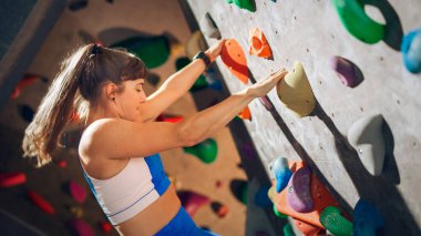 Sporcu Kadın Kaya Tırmanışı Spor Salonundaki Kayalık Duvara Tek başına Tırmanma Çalışması. Kapalı Spor Salonu 'nda Kadın Egzersizleri Sağlıklı Yaşam Tarzı Eğitimi İçin Aşırı Spor Yapıyor. Portreyi Kapat