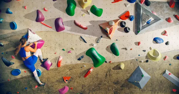 Sporcu Kadın Kaya Tırmanışçısı Spor Salonunda Tek başına Bouldering Wall 'a tırmanıyor. Kapalı Spor Salonu 'nda Kadın Egzersizleri Sağlıklı Yaşam Tarzı Eğitimi İçin Aşırı Spor Yapıyor. Arkadan çekim.