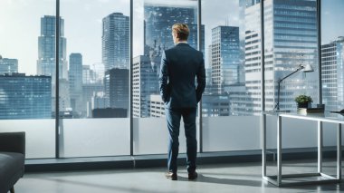 Modern ofisinde dikilip gökdelenlerle Büyük Şehir 'in penceresinden dışarı bakan, Kusursuz Terzi Takımlı Genç İşadamı. Başarılı Finans Yöneticisi Proje Planlama Stratejisi.