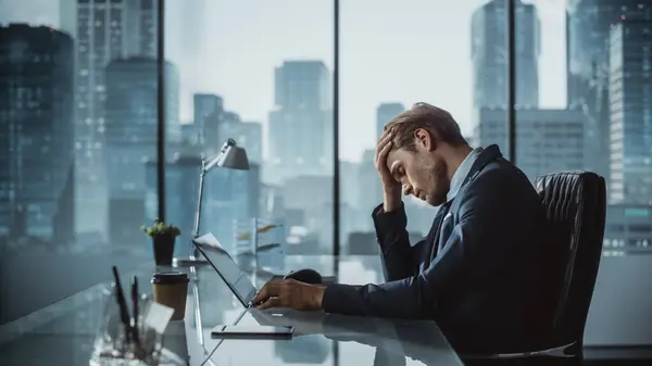 Stressaantunut Liikemies Puvussa Istuu Työpöydällä Modernissa Toimistossa Käyttäen Kannettavaa Tietokonetta — kuvapankkivalokuva