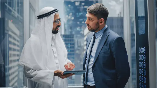 European Businessman Talking Arab Investment Partner While Riding Glass Elevator — Stock Photo, Image