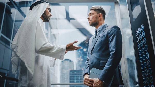 Businessman Talking with Arab Investment Partner while Riding Glass Elevator to Office in a Modern Business Center. International Corporate Associates