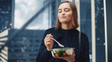 Kendine güvenen genç bir kadının portresi camdan asansörle Modern İş Merkezi 'ndeki ofisine ve sebzeli sağlıklı salata yiyerek. Mutlu Yönetici