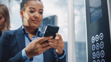 İş Merkezindeki Siyah Yetişkin Kadın Kalabalık Cam Asansörü 'nü kapatın. Akıllı Telefon kullanarak Başarılı Afrikalı Amerikan Yöneticisi, Yaz