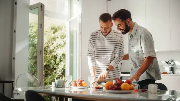 厨房区穿着休闲装的年轻貌美的男同性恋夫妇呆在家里 英俊的男性切苹果和准备午餐 伴侣之间的对话 — 图库照片