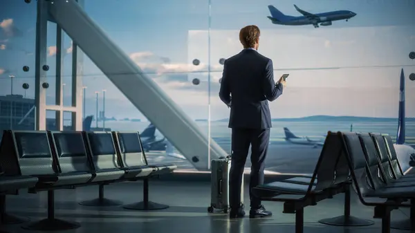 Аэропорт Терминал Бизнесмен Rolling Suitcase Walks Использует Смартфон Приложение Электронного Стоковое Изображение