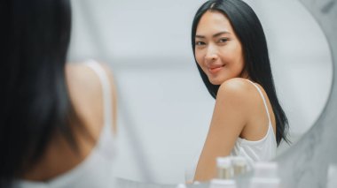 Güzel Asyalı Kadın Mükemmel Yumuşak Omzuna, Boynuna, Aynadaki Duygusal Gülümsemesine Dokunuyor. Mutlu Kadın Güzellik rutininin tadını çıkarıyor. Zindelik