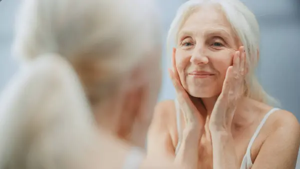 Beautiful Senior Woman Looks Bathroom Mirror Touches Her Face Happily Stock Photo