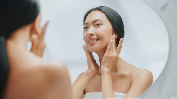 美丽的亚洲女人在浴室镜中轻柔地应用面霜的肖像 年轻的成年女性使她的皮肤柔软 光滑与自然 — 图库照片