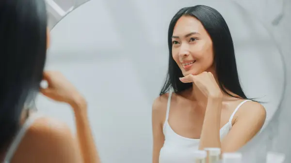 아시아 Admires 그녀의 부드러운 피부와 화려한 카메라와 화장실 거울에서 미소를 스톡 사진