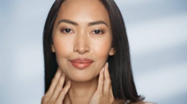 Kadın Güzellik Portresi. Güzel Asyalı mutlu esmer kadın pozu, yüzüne doğal ve sağlıklı bir tenle dokunuyor. Sağlık ve Cilt Bakımı