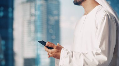 Modern Ofisinde Bekleyen Geleneksel Beyaz Kandura 'daki otantik Müslüman İşadamı Gökdelenli Akıllı Telefonu Kullanıyor. Başarılı.
