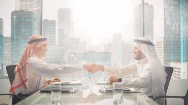Two Successful Emirati Businessmen in White Traditional Kandura Sitting in Office and Signing Contract. Business Partners Shake Hands on Lucrative clipart