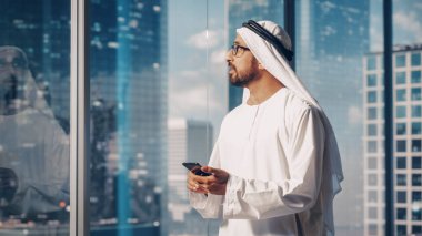 Modern Ofisinde Bekleyen Geleneksel Beyaz Kandura 'daki otantik Müslüman İşadamı Gökdelenli Akıllı Telefonu Kullanıyor. Başarılı.