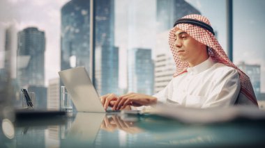 Genç başarılı Arap İş Adamı Beyaz Geleneksel Kandura Ofiste Oturuyor ve Dizüstü bilgisayar üzerinde çalışıyor. İş Yöneticisi Planlama Yatırımları