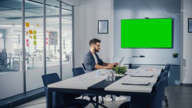 Ofis Konferans Odası: Laptop üzerinde çalışan yakışıklı İspanyol Uzman Yeşil Ekran Choma Key Wall TV ile etkileşim kuruyor. İş adamı