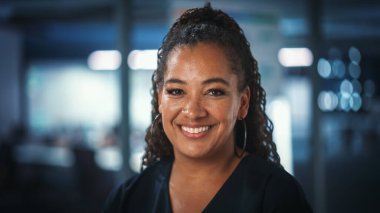 Kendinden emin, mutlu, orta yaşlı, siyah giyinmiş, kameraya bakan, poz veren ve gülümseyen Afro-Amerikan kadınının portresi.