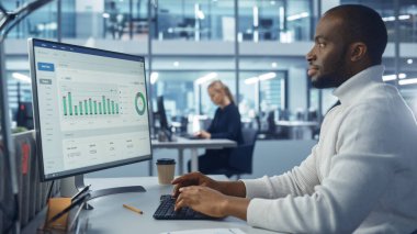 Şirket Ofisi: Büyük Veri İstatistikleri ve Grafikleri ile Yakışıklı Siyah Bilgi İşlem Uzmanı Masaüstü Bilgisayarını Kullanıyor. E-Ticaret üzerine Yaratıcı Yazılım Mühendisi Çalışması