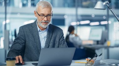 Modern Ofis: Başarılı Orta Çağ Sakallı İşadamı Portresi Masasında Dizüstü bilgisayarla çalışıyor, gülümsüyor. Çeşitli İş Yerleri