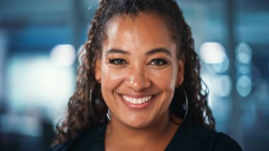 Kendinden emin, mutlu, orta yaşlı, siyah giyinmiş, kameraya bakan, poz veren ve gülümseyen Afro-Amerikan kadınının portresi.