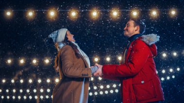 Romantik Kış Karlı Gecesi: Buz pateni yapan çift buz pateni pistinde eğleniyor. Çift Paten Erkek Arkadaşı ve Kız Arkadaşı Seviyor, Dans Ediyor, El Tutuyor, Sarılıyor