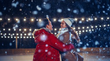 Romantik Kış Karlı Gecesi: Buz pateni yapan çift buz pateni pistinde eğleniyor. Çift Paten Erkek Arkadaşı ve Kız Arkadaşı Seviyor, Dans Ediyor, El Tutuyor, Sarılıyor