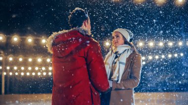 Romantik Kış Karlı Gecesi: Buz pateni yapan çift buz pateni pistinde eğleniyor. Açık havada çift buz pateni. Güzel Gençler Kucaklaşın. Erkek Arkadaş Portresi