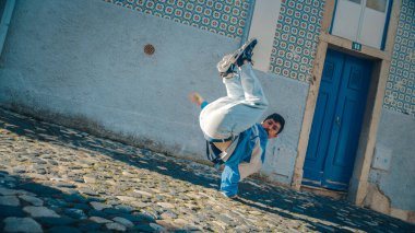 Şık Giyimli Aktif ve Neşeli Genç Latin Adam Eski Bir Şehrin Caddesinde Aktif Bir Breakdance Yapıyor. Bir Şehirdeki Sahne Çekimi