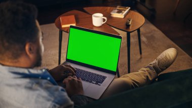 Yeşil Ekran Mock Up Ekranı ile Evden Çalışan Genç Afrikalı Amerikalı Adam. Yaratıcı Erkek Koltukta Oturuyor, Sosyal Hizmetleri Kontrol Ediyor