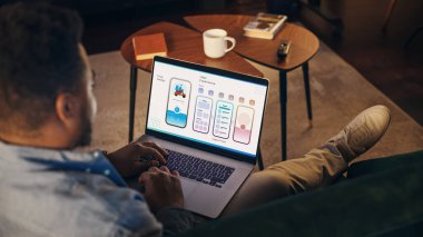 Dizüstü bilgisayarda çalışan, Stylish Loft Apartmanındaki koltukta oturan genç Afrikalı Amerikalılar. Yaratıcı Tasarımcı UX, Yeni Kullanıcı Arayüzü geliştiriyor