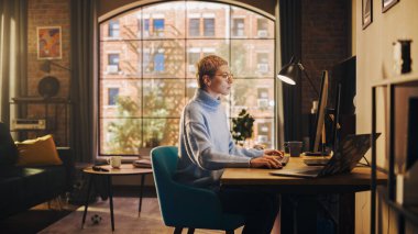 Sunny Stylish Apartmanında Masaüstü Bilgisayarından Çalışan Genç Çekici Kadın. Yaratıcı Tasarımcı Sade Mavi Süveter ve Gözlük Giyiyor