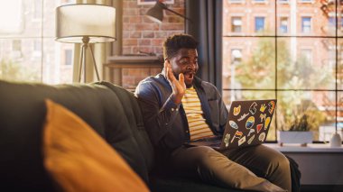 Yakışıklı Afrikalı Amerikalı Sunny Stylish Apartmanında dizüstü bilgisayardan video görüşmesi yapıyor. Arkadaşlarla, meslektaşlarla Yaratıcı İnsan Konuşuyor