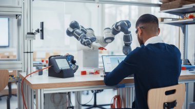 Erkek Endüstriyel Robot Mühendisi Dizüstü Bilgisayarı kullanarak Robot Kolu Kaldırma ve Hareketli Nesneler İçin Yönlendiriyor. Siyah Adam Dokunma Kontrolörü