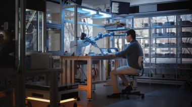 Profesyonel Genç Geliştirici Kodlama Dizüstü bilgisayarda ve Fabrika Atölyesi sırasında Robotik Kol Manipülasyonu. Otomatik Robot Sistemleri Tasarlayan İnsanlar