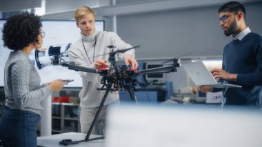 Çeşitli Mühendislerin Beyin Fırtınası ve Dizüstü Bilgisayar Kullanımı. Beyaz erkek modern drone 'u kuruyor. Meslektaşlar Yapılandırma, Yapılandırma ve Test Makineleri