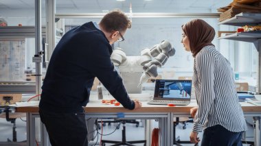 Kıdemli Erkek Mühendis Müslüman Kadın Bilgisayar Bilimleri Uzmanına Kontrolleri Açıklıyor ve Araştırma Laboratuvarında Robotik El 'e İşaret Ediyor