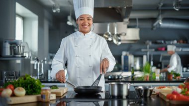 Restaurant Kitchen: Portrait of Black Female Chef in Action, Uses Pan to Cook Delicious, Traditional Authentic Food, Looks at Camera and Smiles
