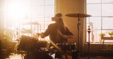 Portrait of a Young Female Wearing a Virtual Reality Headset, Playing Drums in at Home with Warm Sunlight. Drummer Girl Recording Herself Playing