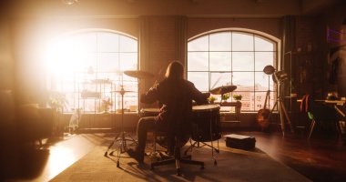 Person Sitting with Their Back to Camera and Playing Drums During a Band Rehearsal in a Loft Studio with Sunlight. Drummer Practising Alone Before a
