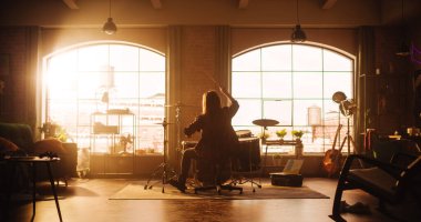 Person Sitting with Their Back to Camera, Playing Drums During a Band Rehearsal in a Loft Studio with Sunlight. Drummer Practising Alone Before a